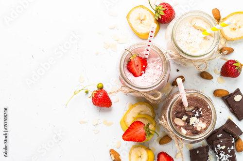 Fotografiet Banana chocolate and strawberry milkshakes in jars on white