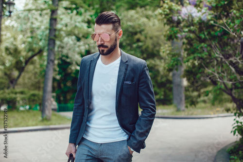 Stylish man with a beard and in sunglasses standing in the park.