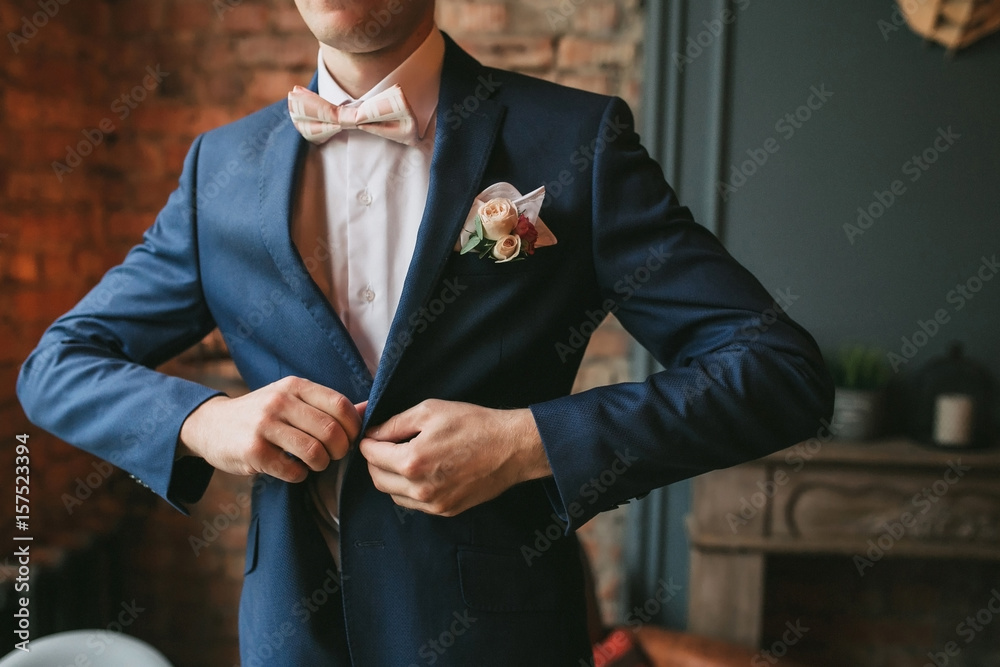 A young groom in a blue suit and a pink bow tie button his jacket against  the backdrop of a brick wall and a fireplace Stock Photo | Adobe Stock