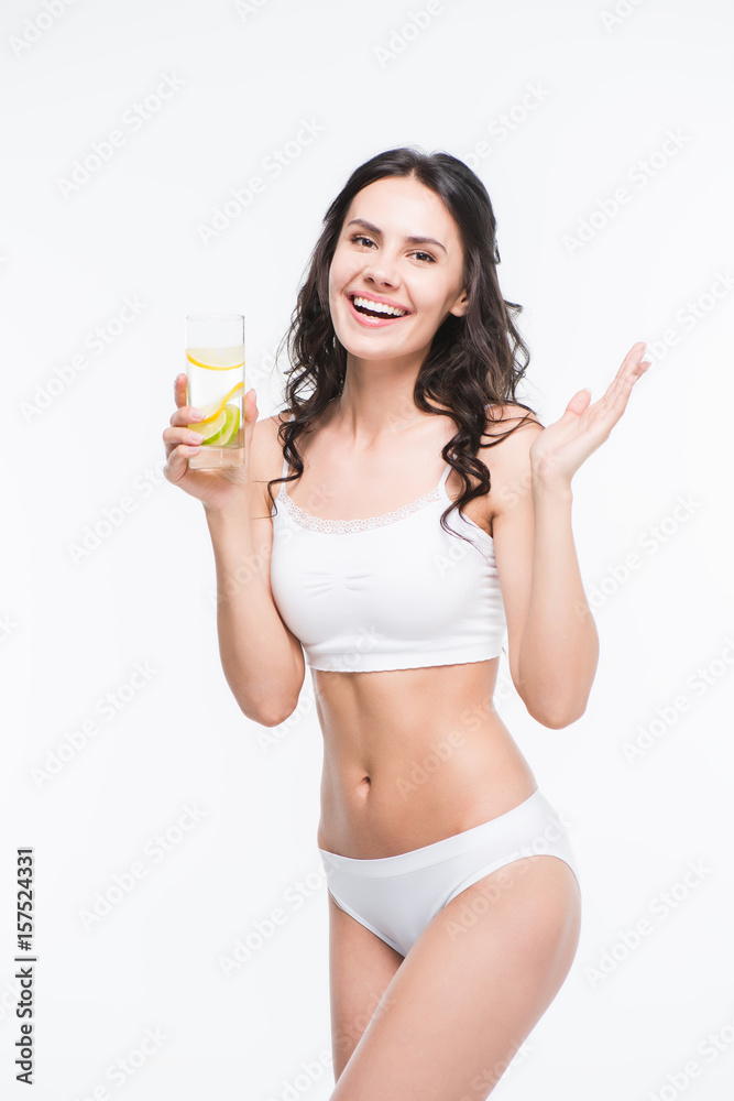 smiling woman in white underwear holding glass of water with lemon and looking at camera smiling woman in white underwear holding glass of water with lemon and looking at camera