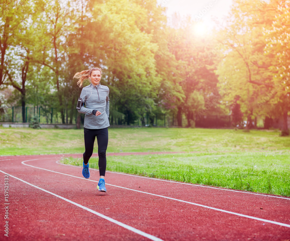 Obraz premium Athletic woman running on track with smart phone app, fitness lifestyle