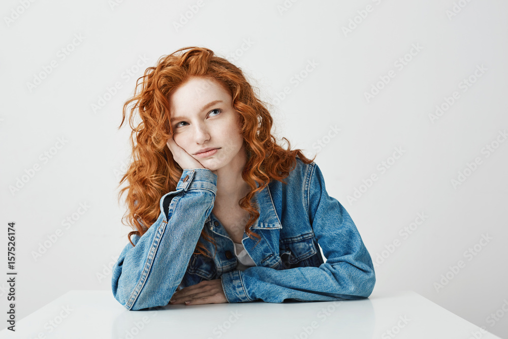 Naklejka premium Dreamy beautiful girl thinking dreaming sitting at table over white background.