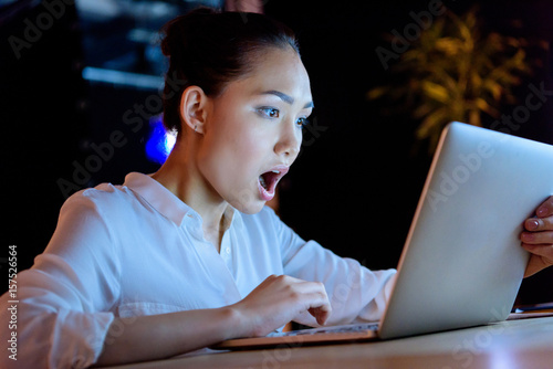 amazed young asian businesswoman working on laptop while sitting at table