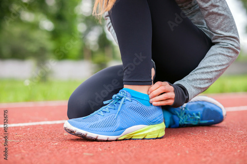 Athletic woman on running track touching hurt leg with ankle injury