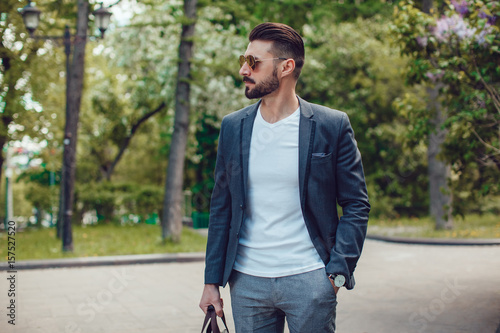 Stylish man with a beard and in sunglasses standing in the park. © kanashkin