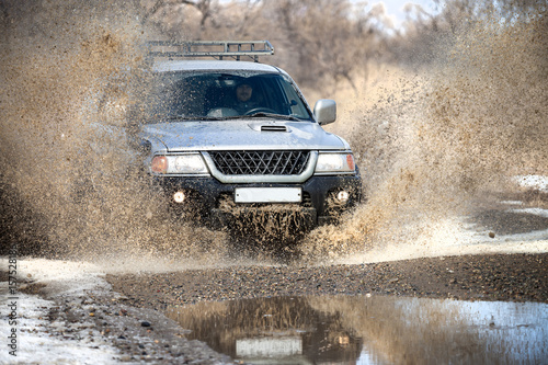 Japanese SUV on dirt road in early spring making splashes from a puddle