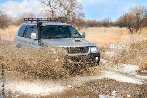 SUV on dirt road in early spring making splashes from a puddle © yo camon