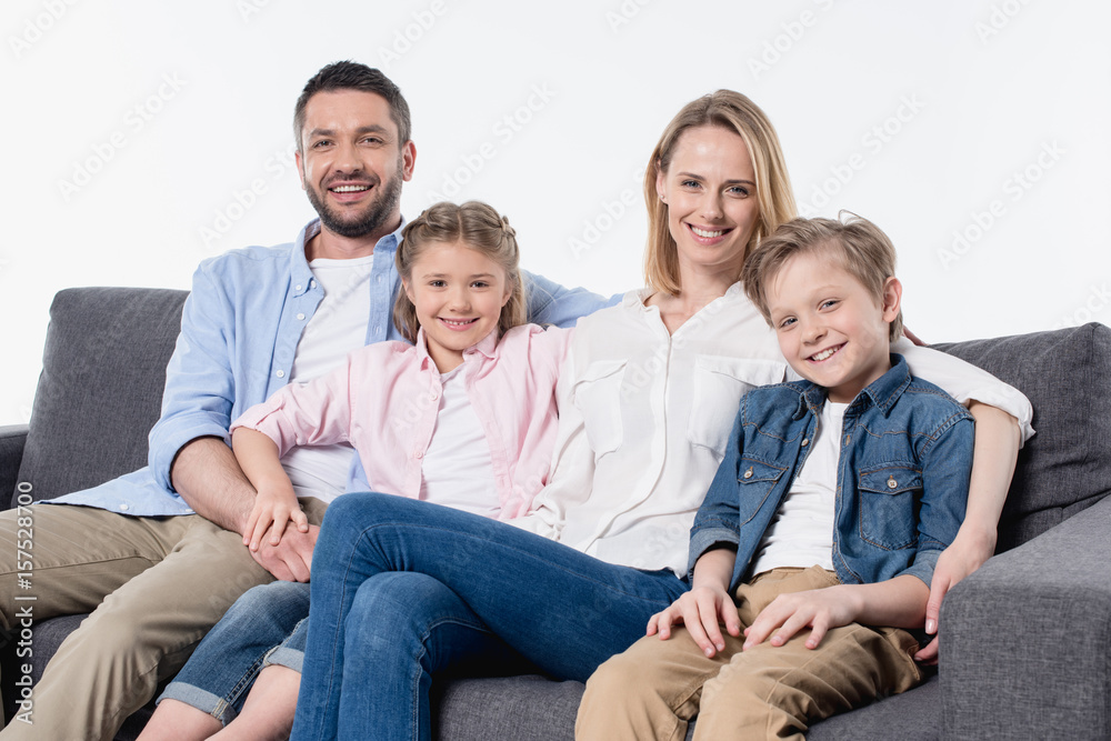 Happy family with two children sitting together on couch and smiling at camera Happy family with two children sitting together on couch and smiling at camera
