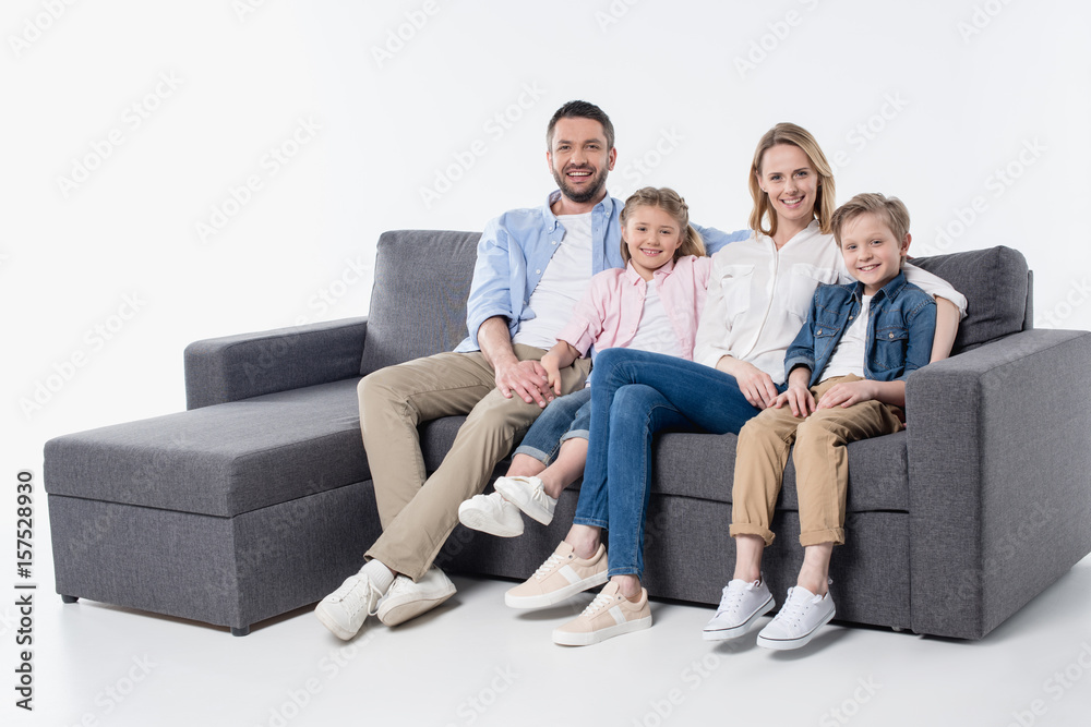 Happy family with two children sitting together on couch and smiling at camera Happy family with two children sitting together on couch and smiling at camera