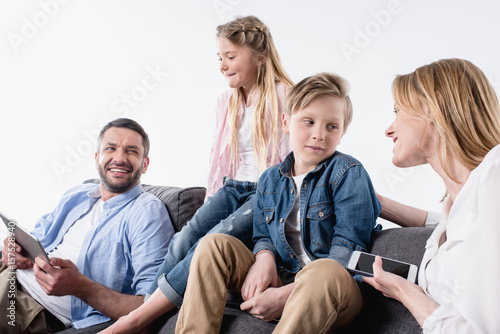 caucasian family with digital devices sitting on sofa together
