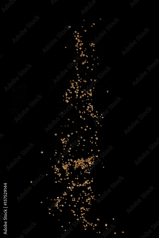 Sifting brown cane sugar over black background. Isolated