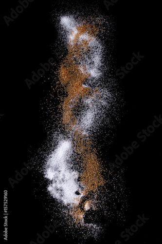 Sifting white and brown cane caster sugar over black background. Isolated