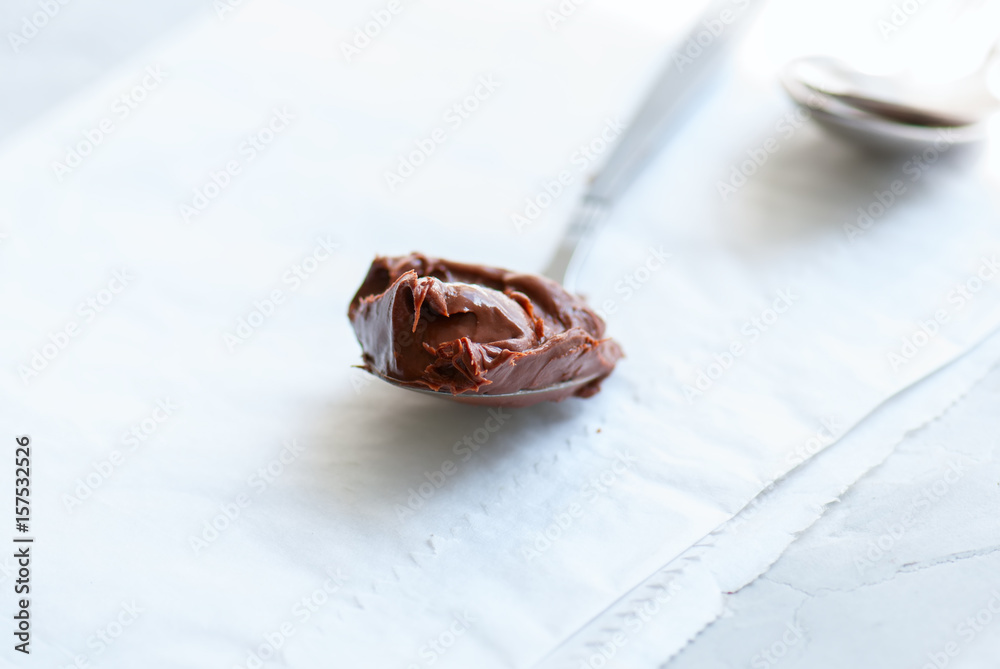 Fototapeta premium Melted chocolate paste in a spoon on a white stone background. Close up and copy space.