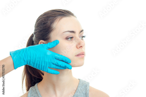a doctor in a blue glove touches the cheek of a young girl without makeup that looks toward close-up
