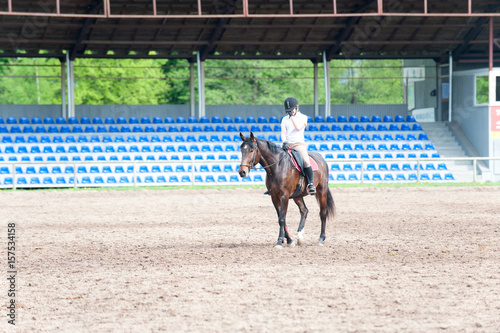 Young teenage girl riding a horse after training on arena