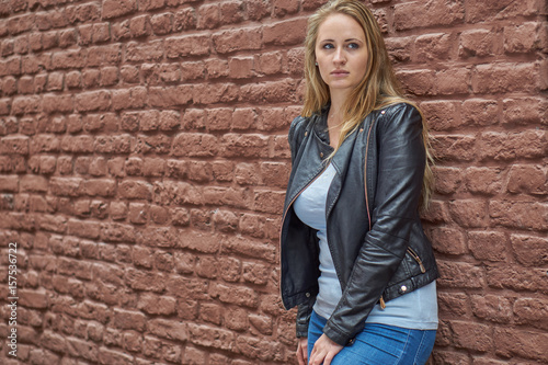 Hübsche blone Frau mit Lederjacke vor roter Backsteinwand photo