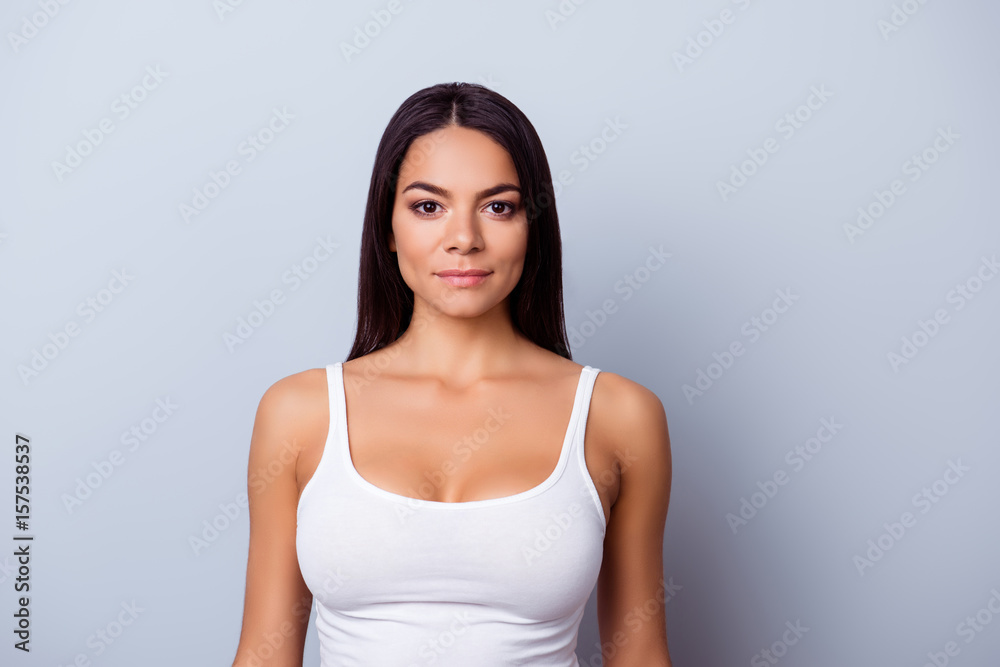 Portrait of a young latino american girl. She is in a casual white singlet standing on the pure light blue background Portrait of a young latino american girl. She is in a casual white singlet standing on the pure light blue background