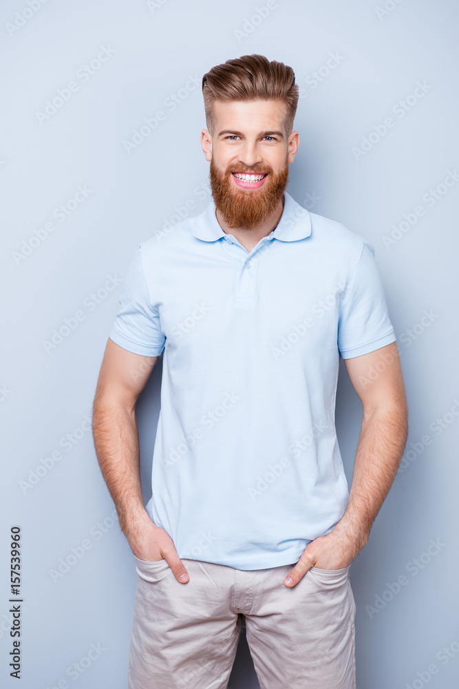 Successful stylish young red bearded man in casual wear is standing on the pure background, has a beaming smile