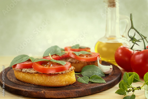 Bruschetta with liver pate, tomatoes and basil on a wooden board. Traditional Italian snack. Close-up.