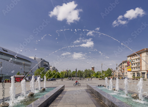 Jets of water from the fountain near the facade of the Administrative Palace of Craiova on Mihai Viteazul square, Craiova, Romania, on a sunny day photo
