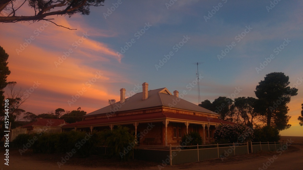 Obraz premium Stone farmhouse nestled in a yard surrounded by trees at sunset. 
