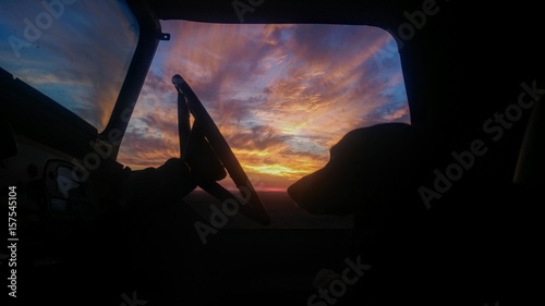 Silhouette of a dog and steering wheel before a stunning sunset in open country. 