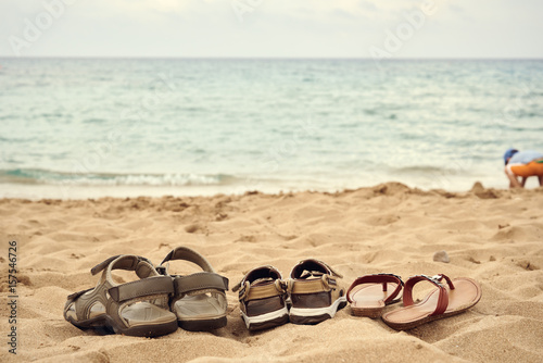Three pairs of sandals on the beach sand. Its belong to father, mother and child The view to the sea.