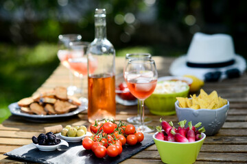 holiday summer brunch party table outdoor in a house backyard with appetizer, glass of rosé wine, fresh drink and organic vegetables