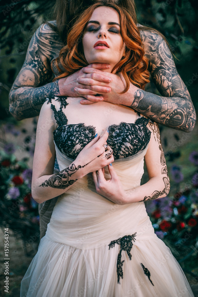 Man with tattoo holding wooman neck in hand. Couple near decorated arch. Fairytale story consept.