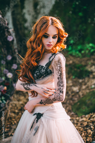Woman portrait outdoor in forest with tattoo and long red hair.