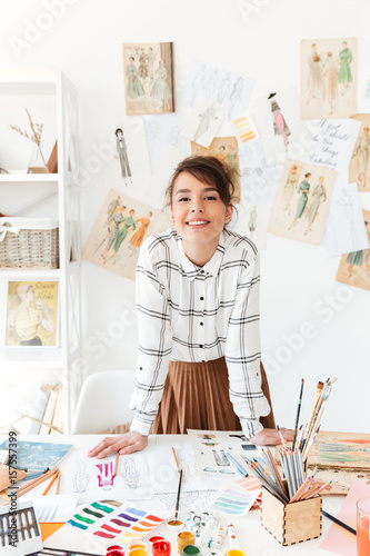 Smiling young woman fashion designer standing at her workplace