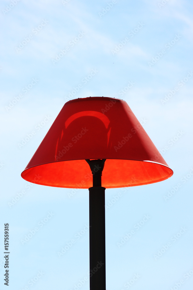 Lantern with a red shade in the courtyard of a residential building against the blue sky.