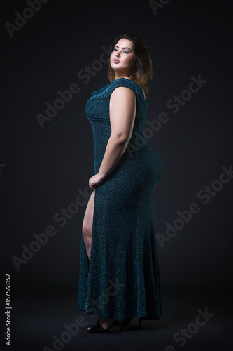 Plus size fashion model in green evening dress, fat woman on black background, overweight female body
