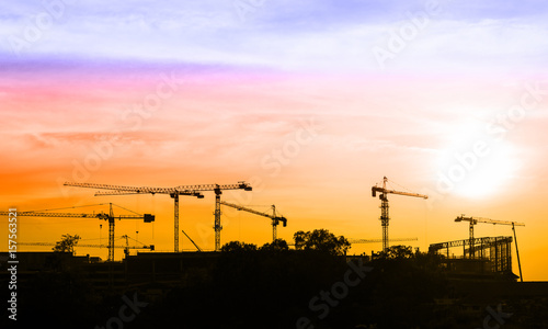 Highrise tower crane lifting the cargo over sunset on colorful sky.