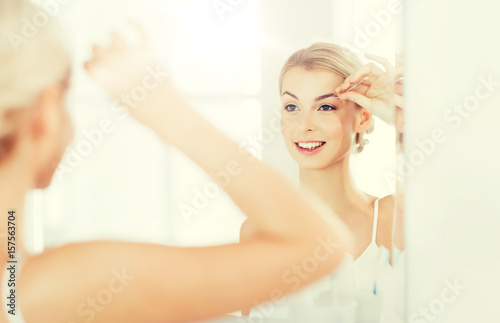 woman with tweezers tweezing eyebrow at bathroom