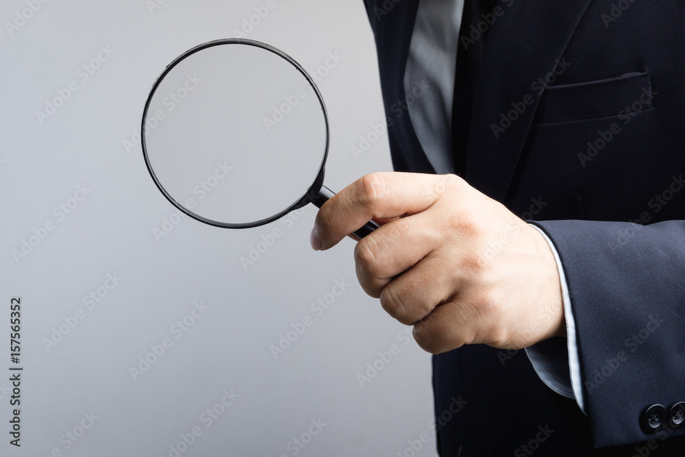 Business man hand holding magnifier for inspection Business man hand holding magnifier for inspection