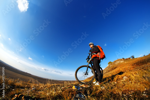 Low, wide angle portrait against blue sky of mountain biker going downhill. Cyclist in black sport equipment and helmet