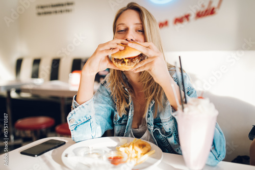 Print op canvas Young woman eating burger in restaurant