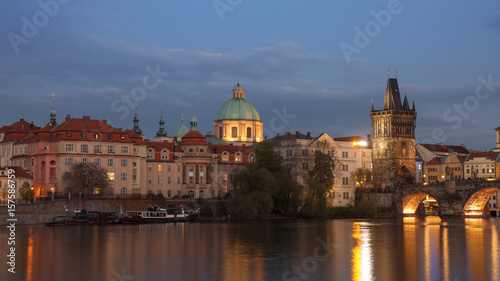 Old Town Bridge Tower and Vltava river bank with Charles bridge after dark. The dome of St. Francis Of Assisi Church in the background. Docked boats of Old Town river bank of Vltava.