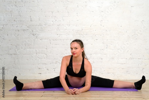 Young pregnant woman doing stretching twine exercises on yoga mat