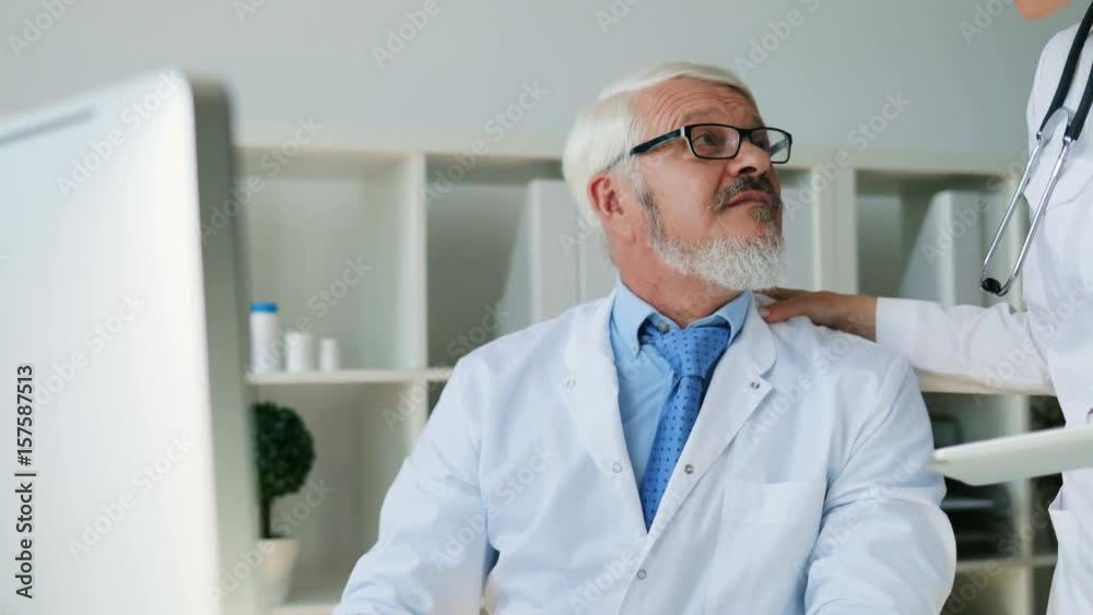 Caucasian young female doctor coming to office of midle aged male doctor and talking about something looked on tablet. Indoor. Caucasian young female doctor coming to office of midle aged male doctor and talking about something looked on tablet. Indoor.