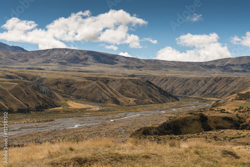 Middle Earth, New Zealand - March 14, 2017: High desert landscape with Lake Clearwater overflow drain to Rangitata River under blue sky with white clouds. Set in brown dry vegetation on mountains.