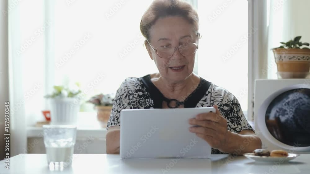 Modern elderly woman using tablet PC in her kitchen Modern elderly woman using tablet PC in her kitchen