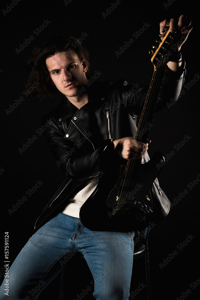 Music and creativity. Handsome young man in a T-shirt, jacket and jeans, with an electric guitar, on a black isolated background. Vertical frame Music and creativity. Handsome young man in a T-shirt, jacket and jeans, with an electric guitar, on a black isolated background. Vertical frame