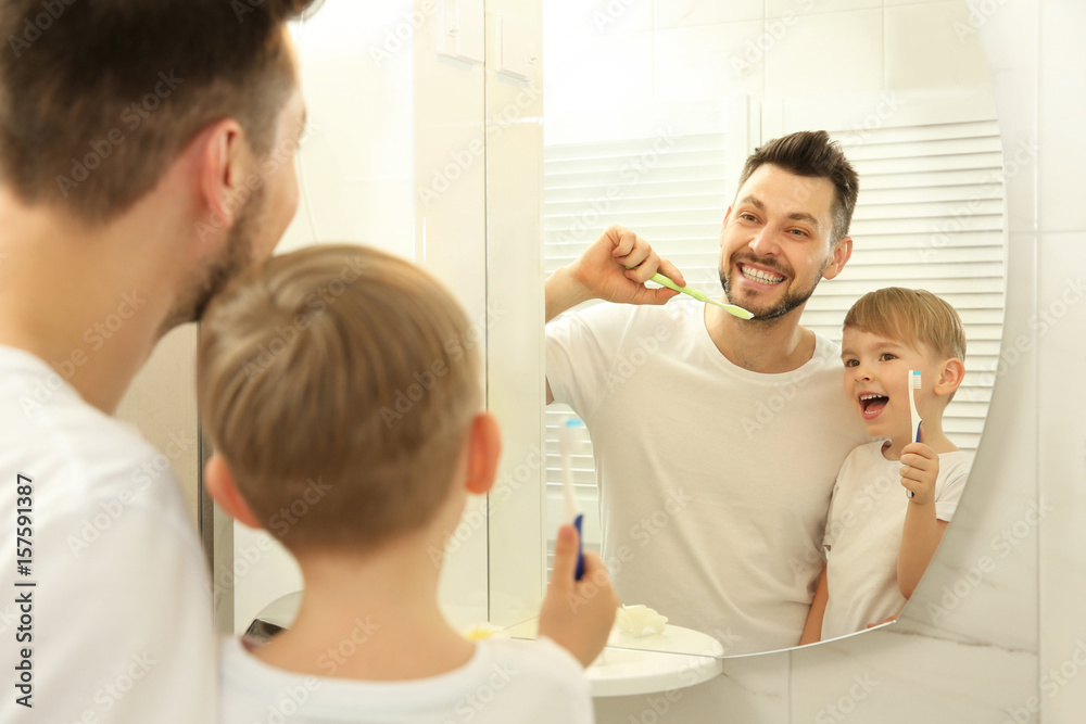 Obraz premium Young father with his son brushing teeth and looking in mirror