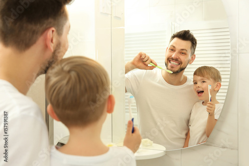 Young father with his son brushing teeth and looking in mirror