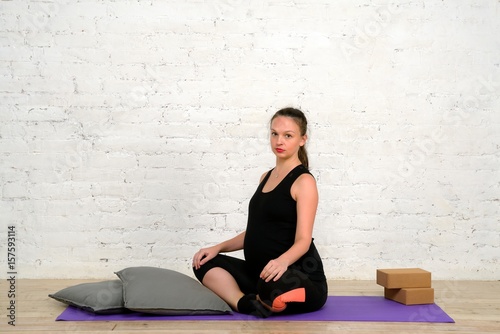 Young pregnant woman sits in lotus position on yoga mat