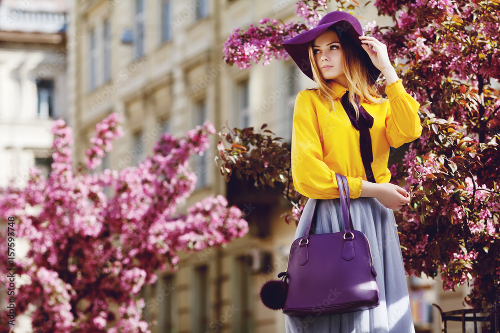 Outdoor portrait of young beautiful girl posing in street. Model wearing stylish hat, shirt, skirt, holding purple bag, handbag. City lifestyle. Female fashion concept. Copy, empty space for text
 - obrazy, fototapety, plakaty 