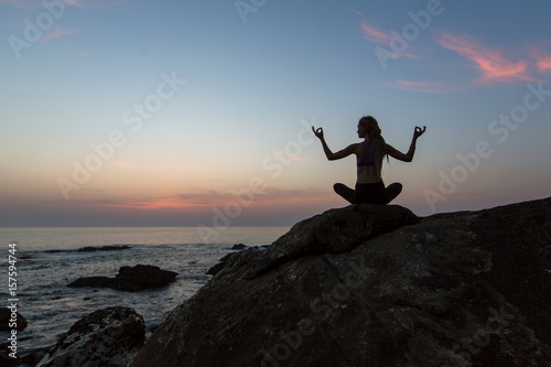Silhouette young woman practicing yoga on the beach at twilight. Meditation.