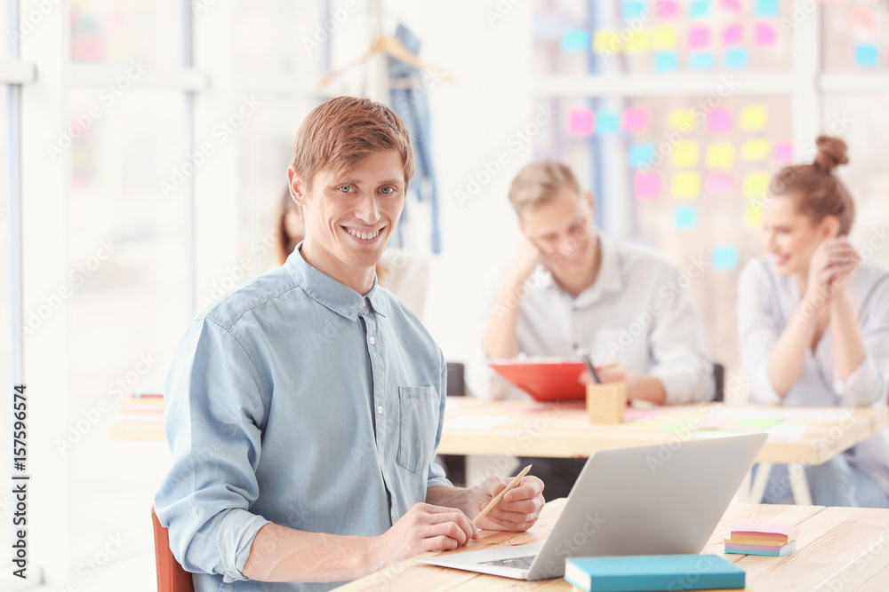 Young man sitting at table and using laptop in office Young man sitting at table and using laptop in office